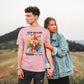 Two people standing in a field with one wearing a pink t-shirt with a colorful graphic and text.