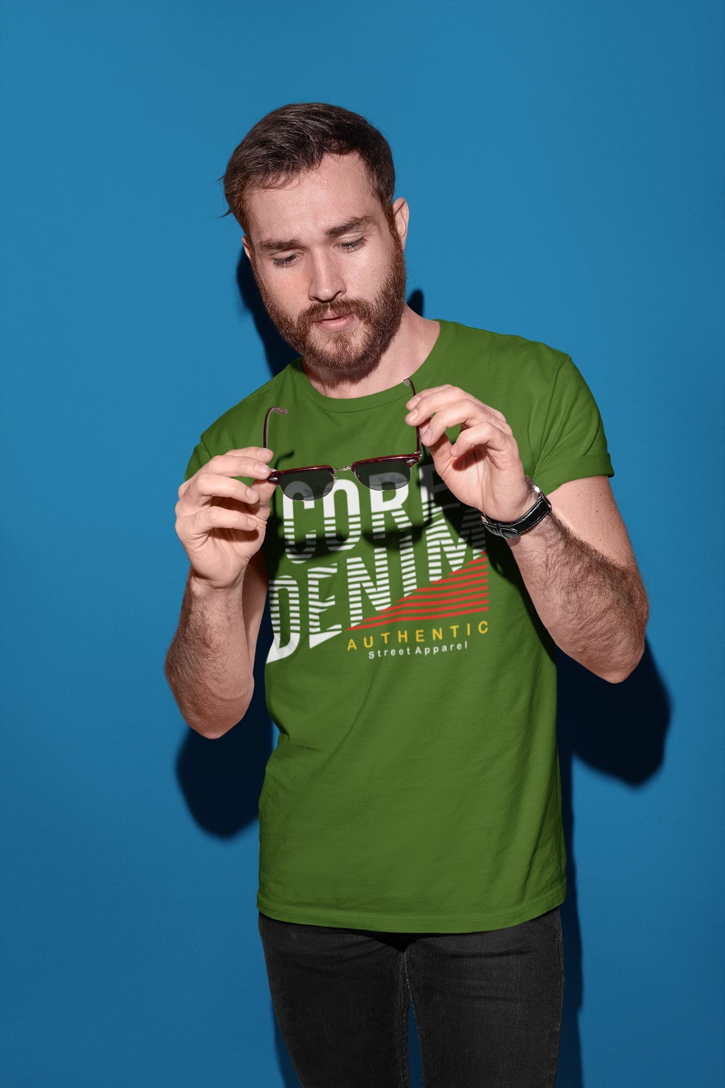 Man wearing a green t-shirt with text, holding sunglasses against a blue background