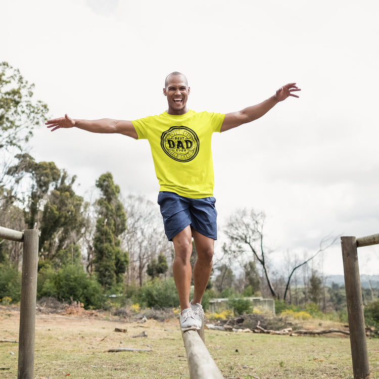 Man balancing on a log outdoors wearing a yellow &