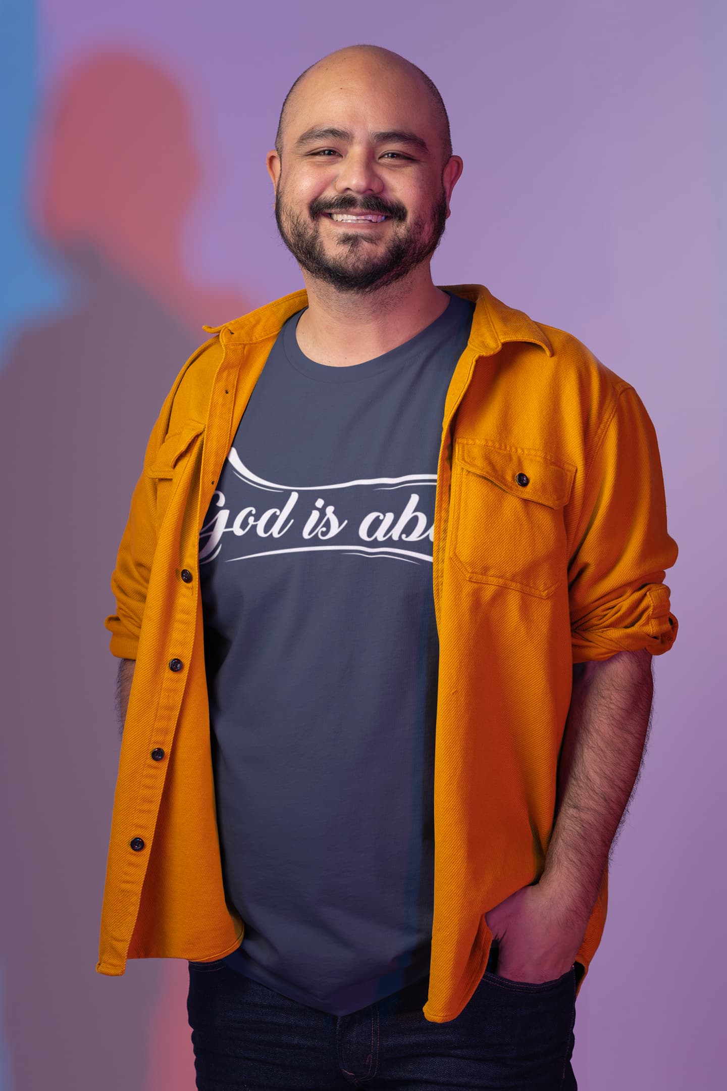 Man wearing an orange shirt over a dark t-shirt with text, standing against a purple background