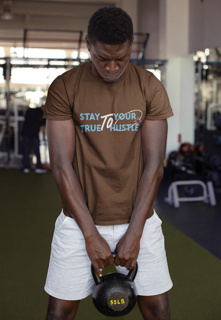 Person lifting a kettlebell in a gym wearing a brown t-shirt with text.