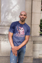 Man wearing a blue t-shirt with a graphic design standing outdoors.