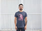 Man wearing a t-shirt with a graphic design and text standing against a white wall.