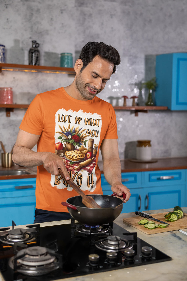 Man cooking in a kitchen wearing an orange t-shirt with a graphic design.