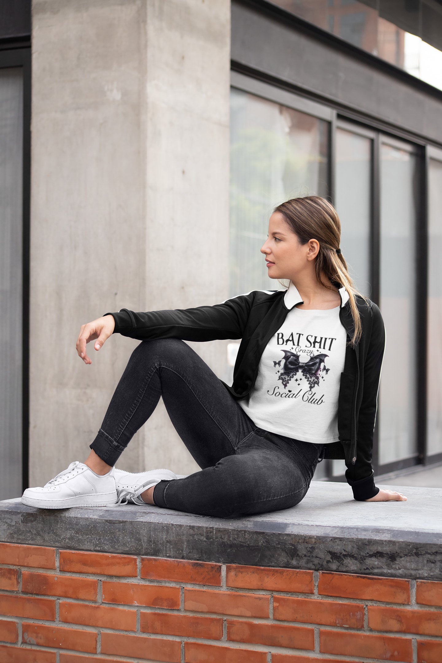 Woman sitting on a ledge wearing a black jacket and white t-shirt with text.