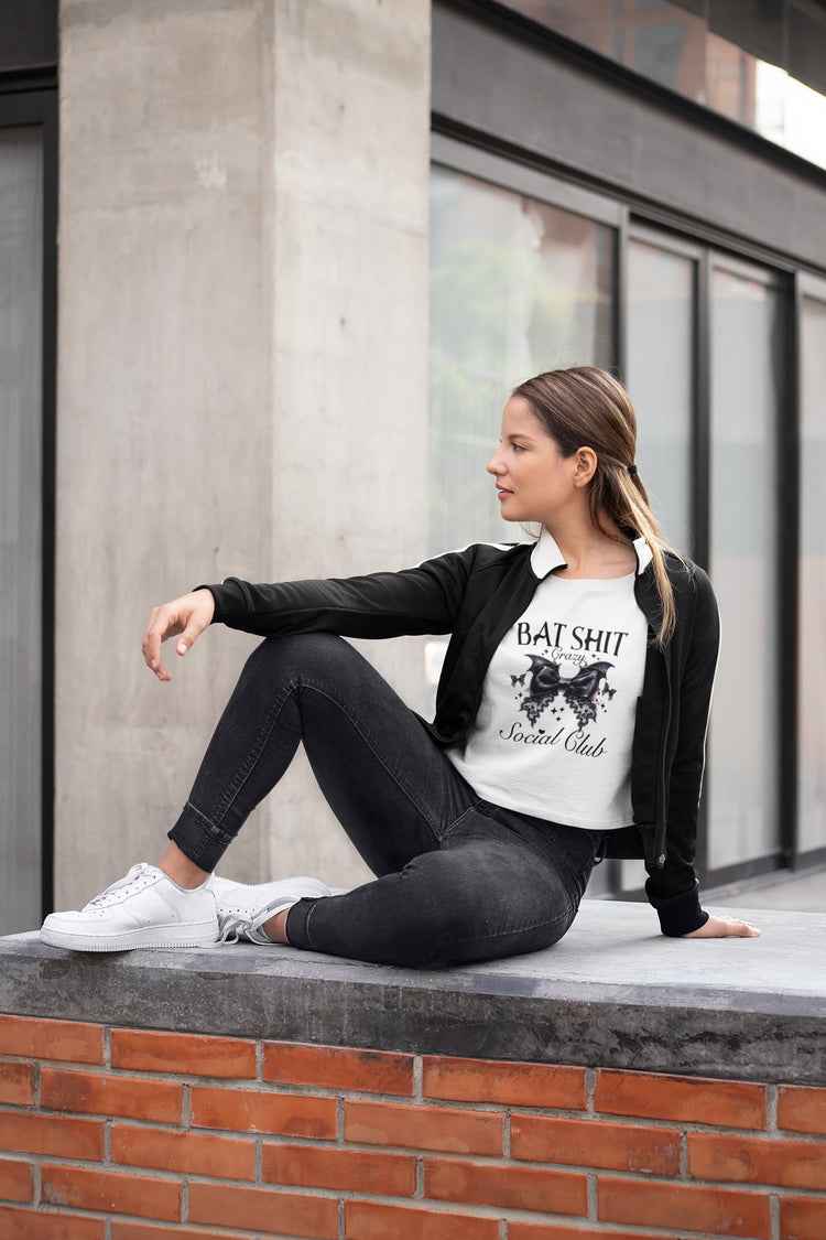 Woman sitting on a ledge wearing a black jacket and white t-shirt with text.