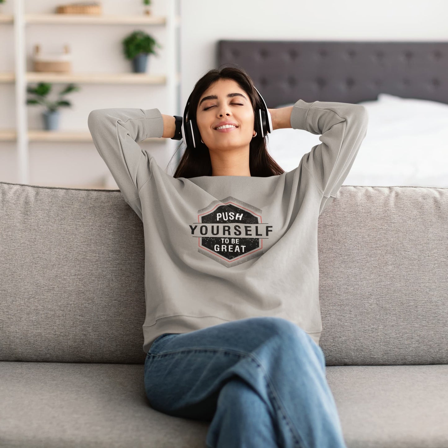 Woman wearing a sweatshirt with 'Push Yourself to be Great' text, sitting on a couch.