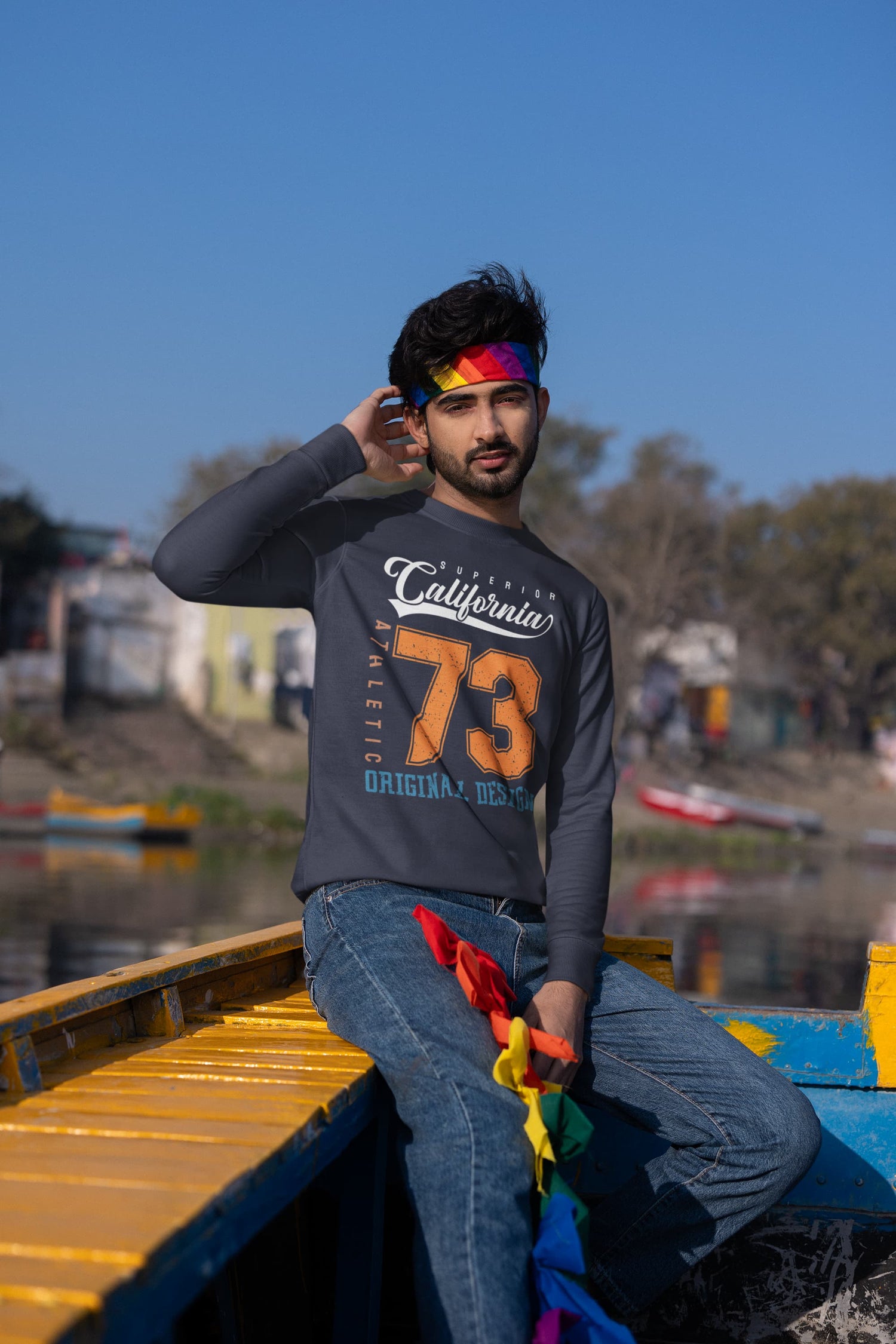 Man sitting on a boat with colorful flags, wearing a dark gray sweatshirt with &