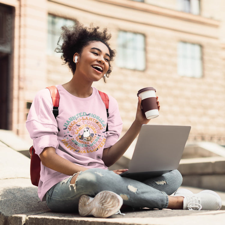 Woman sitting on steps with a laptop and coffee cup, wearing a pink shirt and jeans.