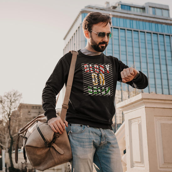 Man wearing a black sweatshirt with text, holding a beige bag, standing in an urban setting.