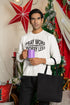 Man holding a purple mug and black bag in a decorated room with Christmas trees and red decorations.