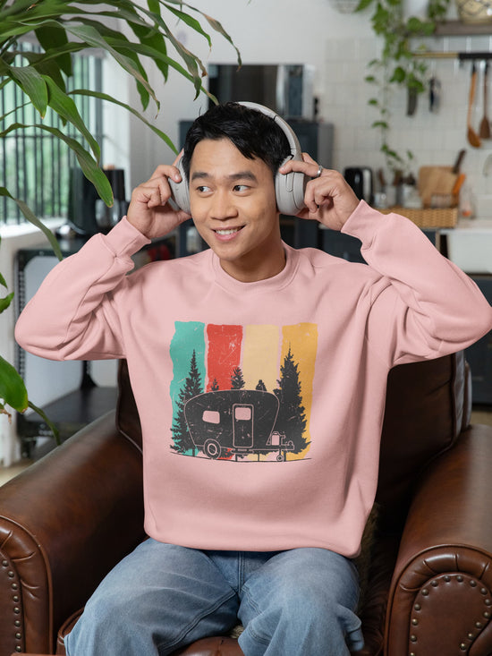 Person wearing a pink sweatshirt with a graphic design, sitting on a couch in a room with plants and kitchen items.