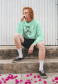 Person wearing a light green sweatshirt with a design, sitting on steps with pink petals around.