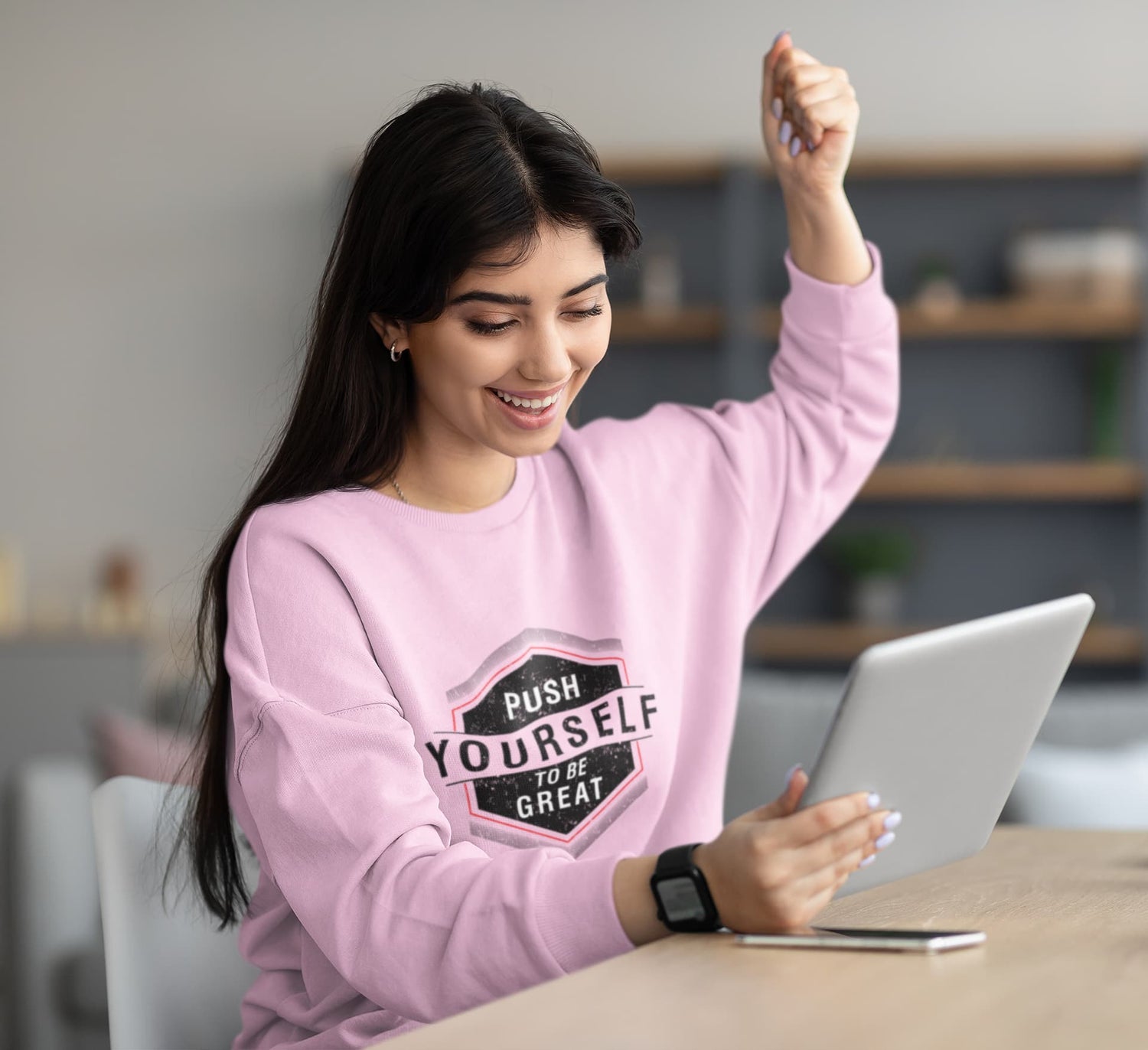 Woman in pink sweatshirt using a laptop with a motivational quote, sitting at a desk.