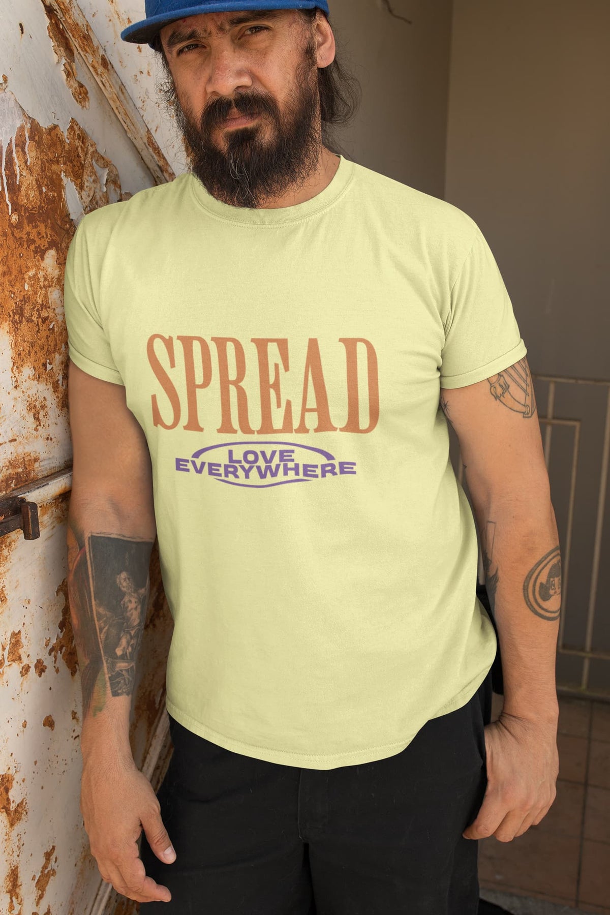 Man wearing a light green t-shirt with 'SPREAD LOVE EVERYWHERE' text, standing against a wall.