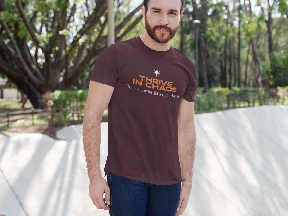 Man wearing a brown t-shirt with 'Thrive in Chaos' text outdoors.