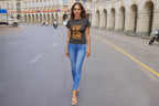 Woman walking on a city street wearing a dark t-shirt with orange text and blue jeans.