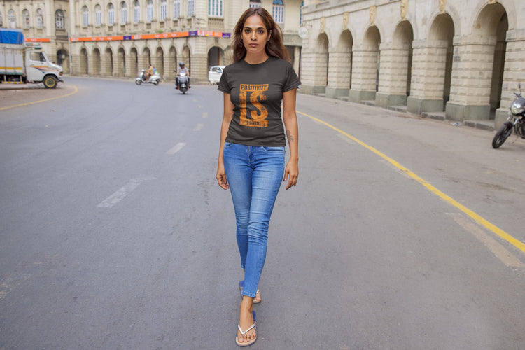 Woman walking on a city street wearing a dark t-shirt with orange text and blue jeans.