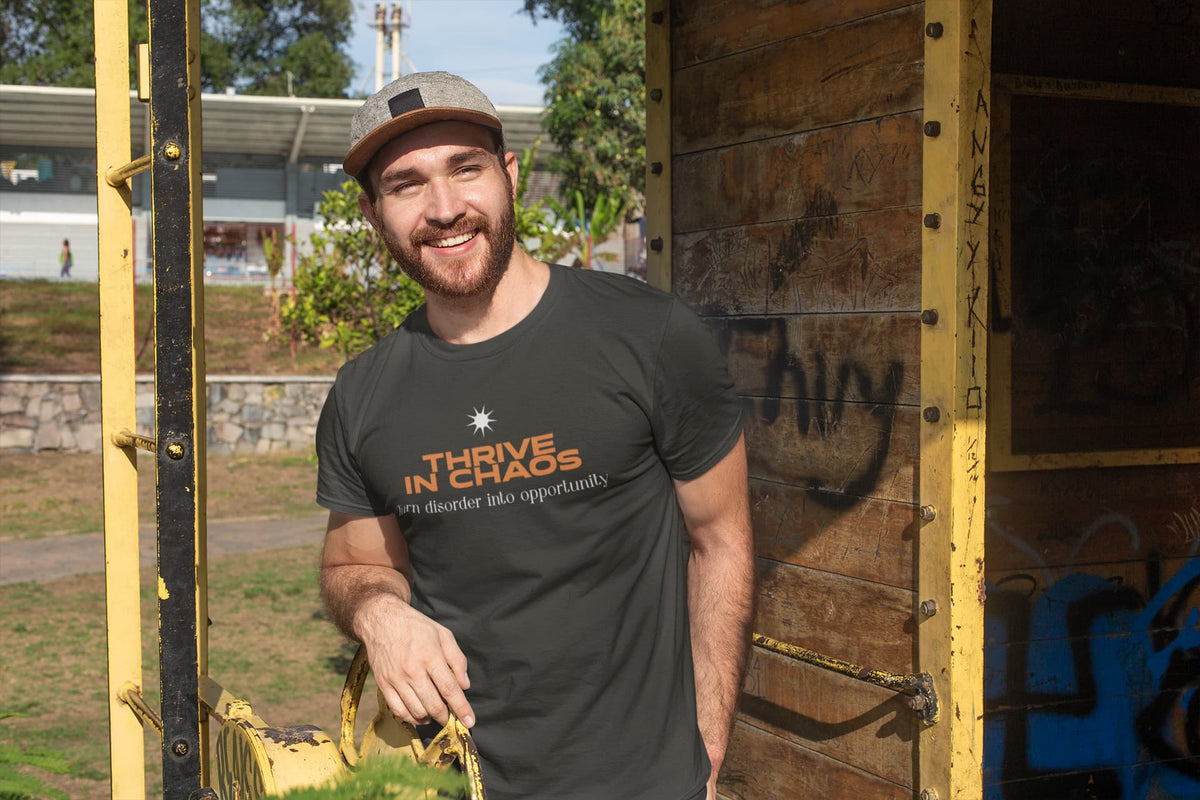Man wearing a 'Thrive in Chaos' t-shirt standing next to a wooden structure with graffiti.