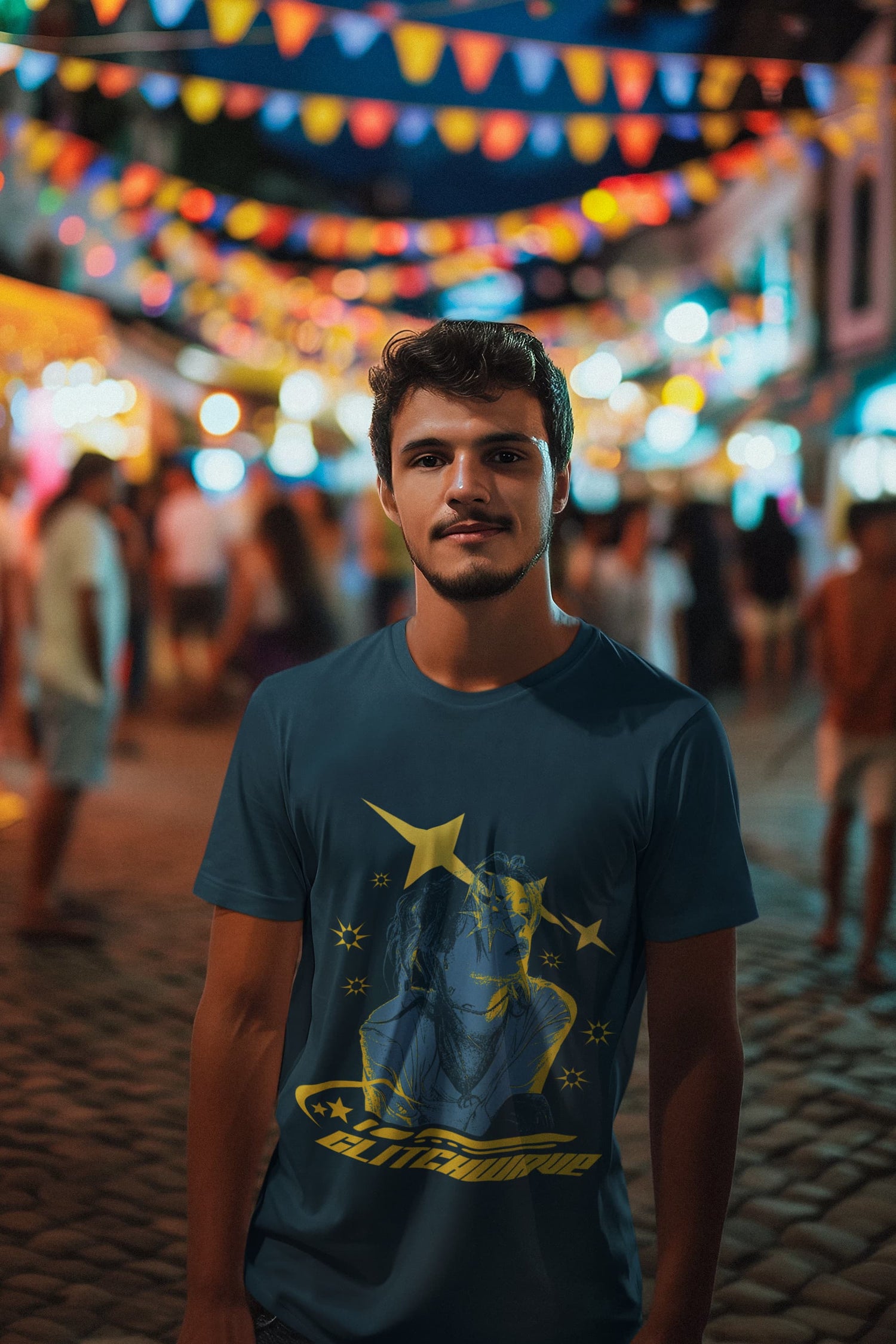 Man wearing a blue t-shirt with a graphic design in a festive outdoor setting with colorful lights and people.
