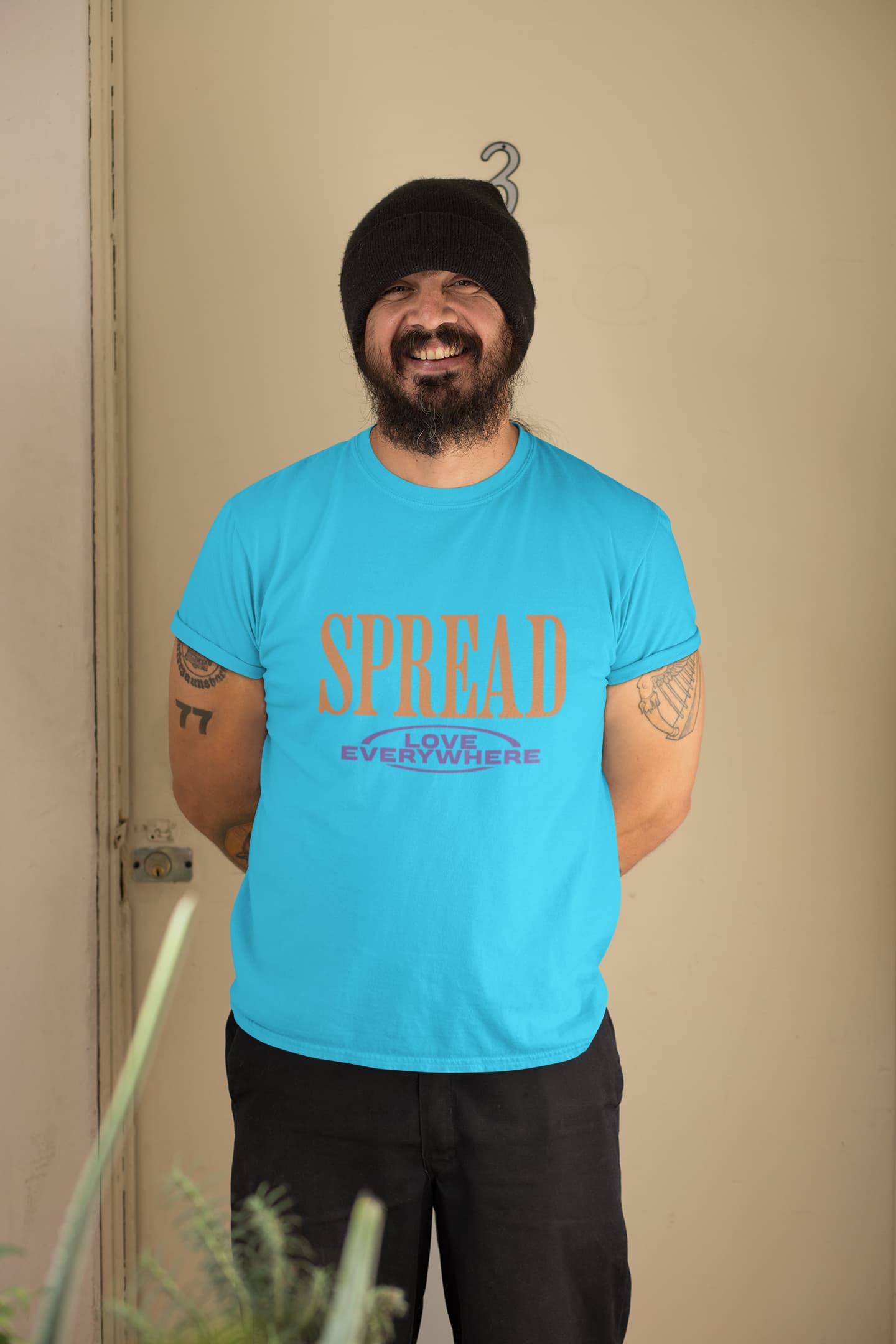 Man wearing a blue t-shirt with 'SPREAD LOVE EVERYWHERE' text, standing against a beige wall.