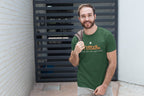 Man wearing a green t-shirt with a logo and text, standing against a brick wall.