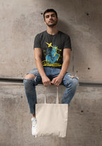 Man sitting on a concrete ledge wearing a graphic t-shirt and holding a tote bag.