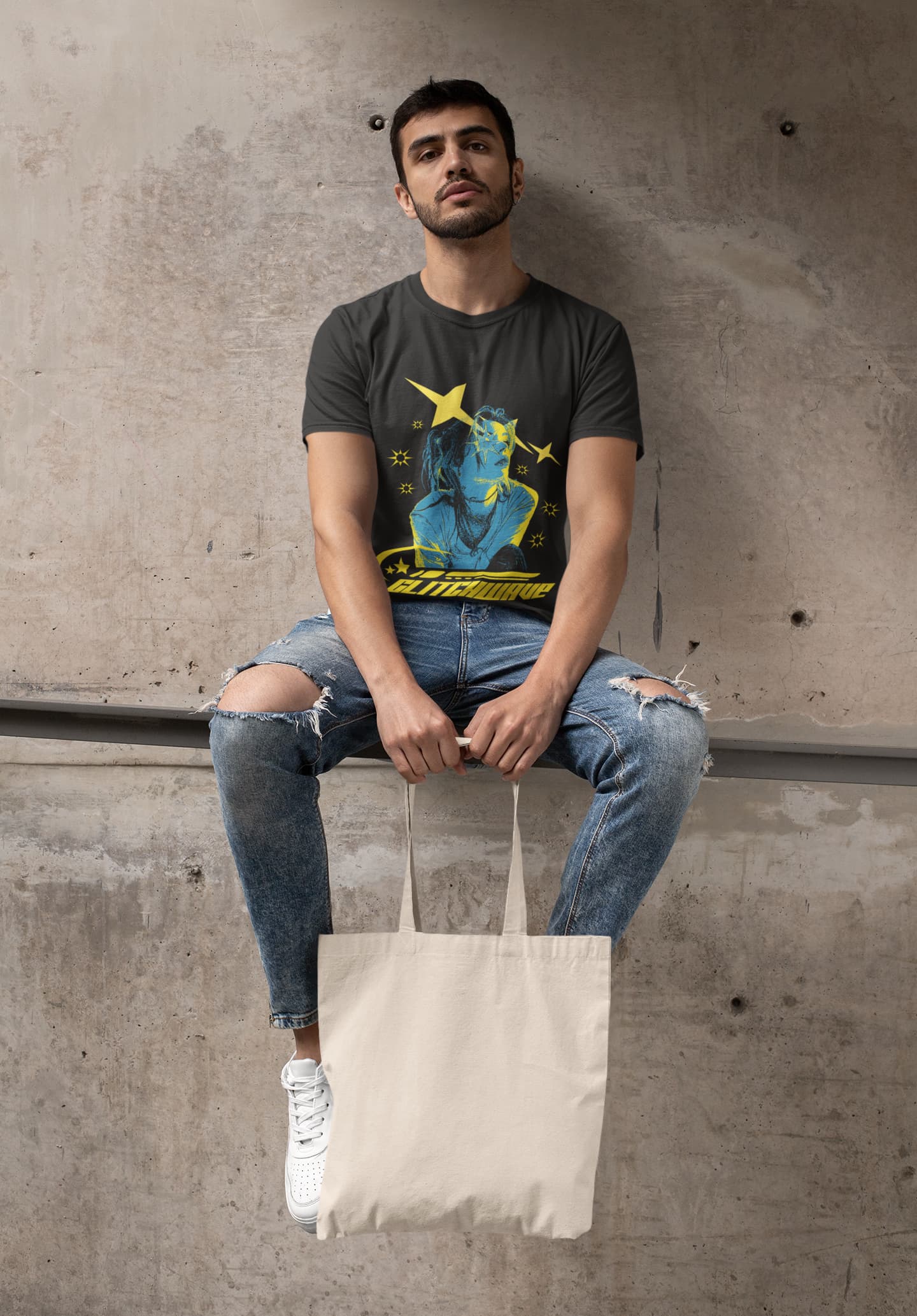 Man sitting on a concrete ledge wearing a graphic t-shirt and holding a tote bag.