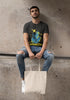 Man sitting on a concrete ledge wearing a graphic t-shirt and holding a tote bag.