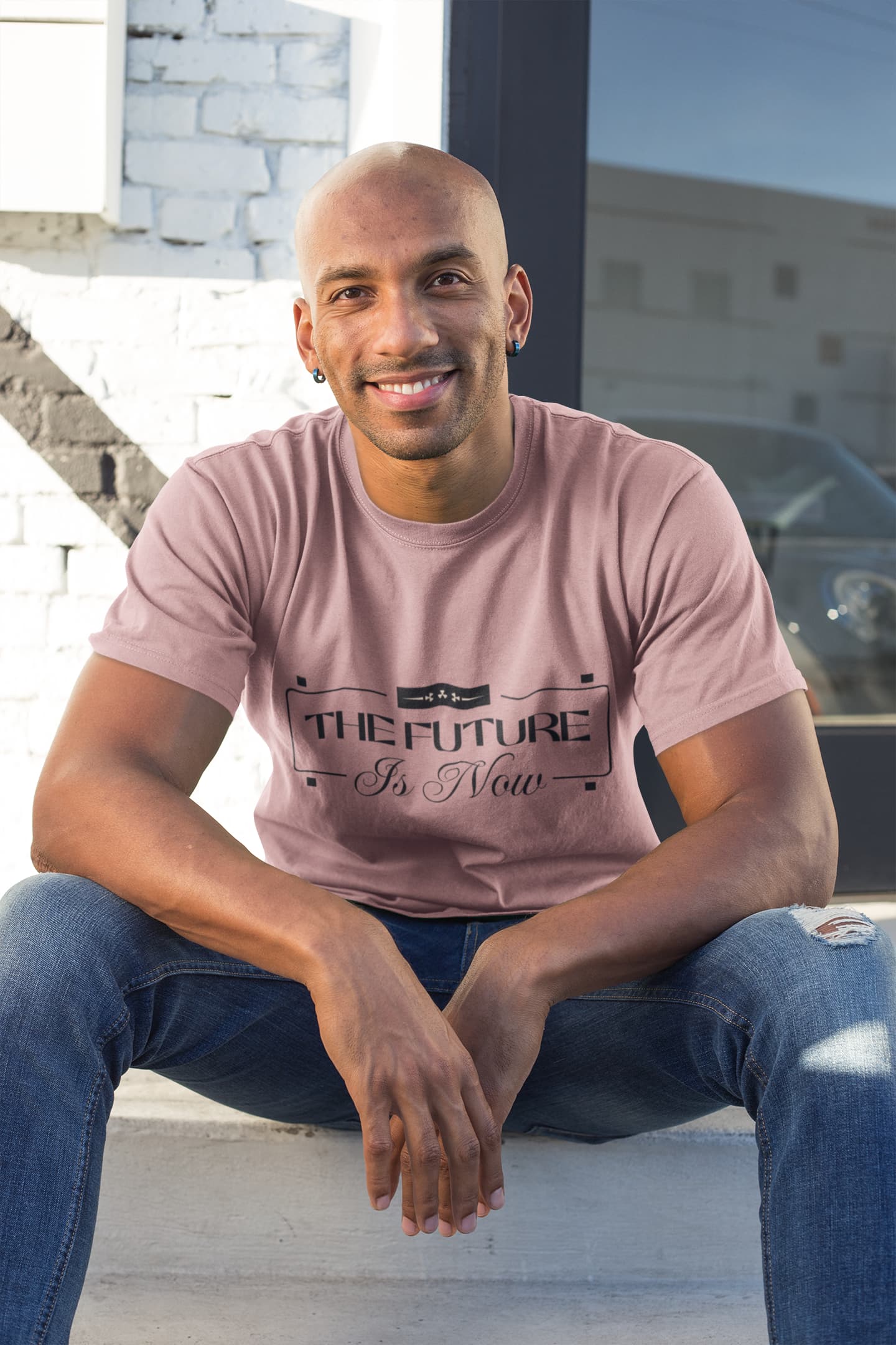 Man wearing a pink t-shirt with text sitting on steps outdoors.