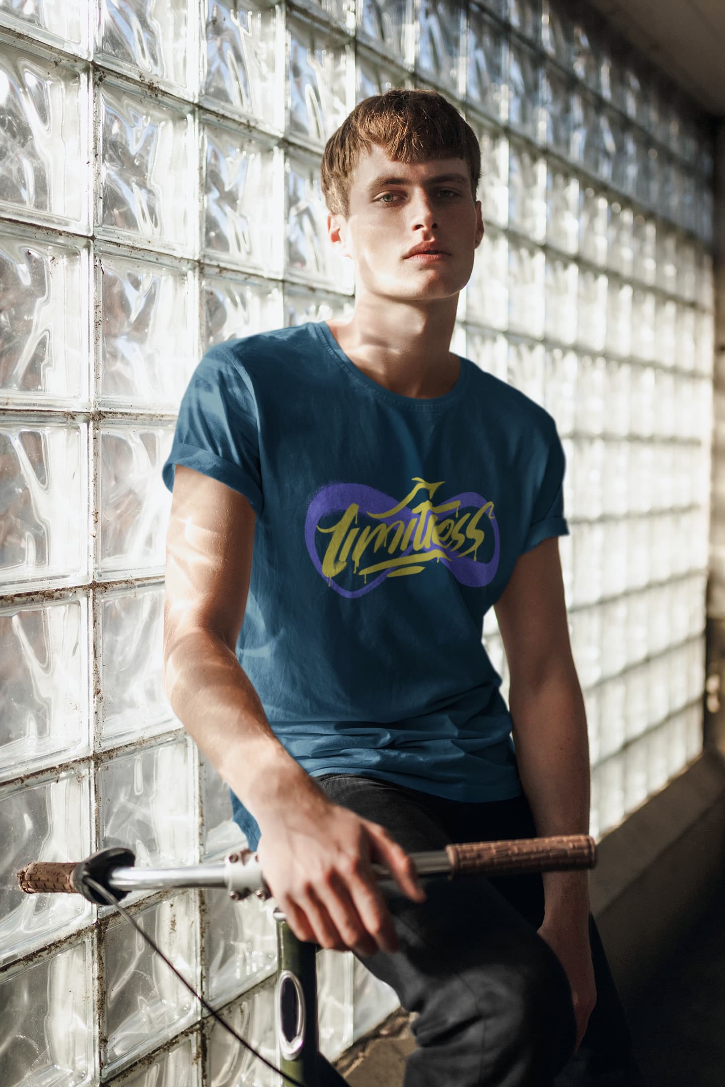 Person wearing a blue t-shirt with a logo, holding a bicycle against a glass block wall.