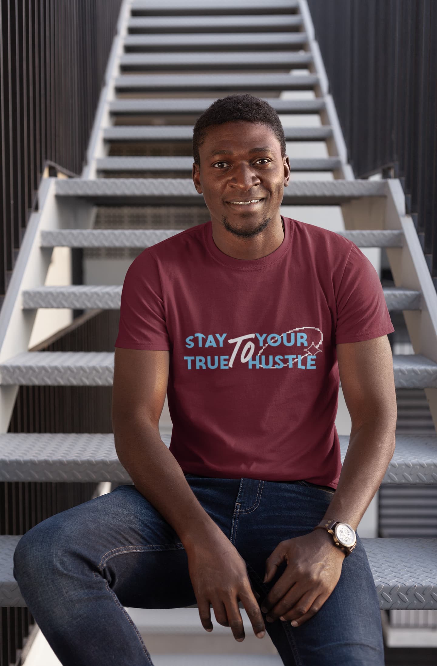 Man wearing a maroon t-shirt with text sitting on stairs