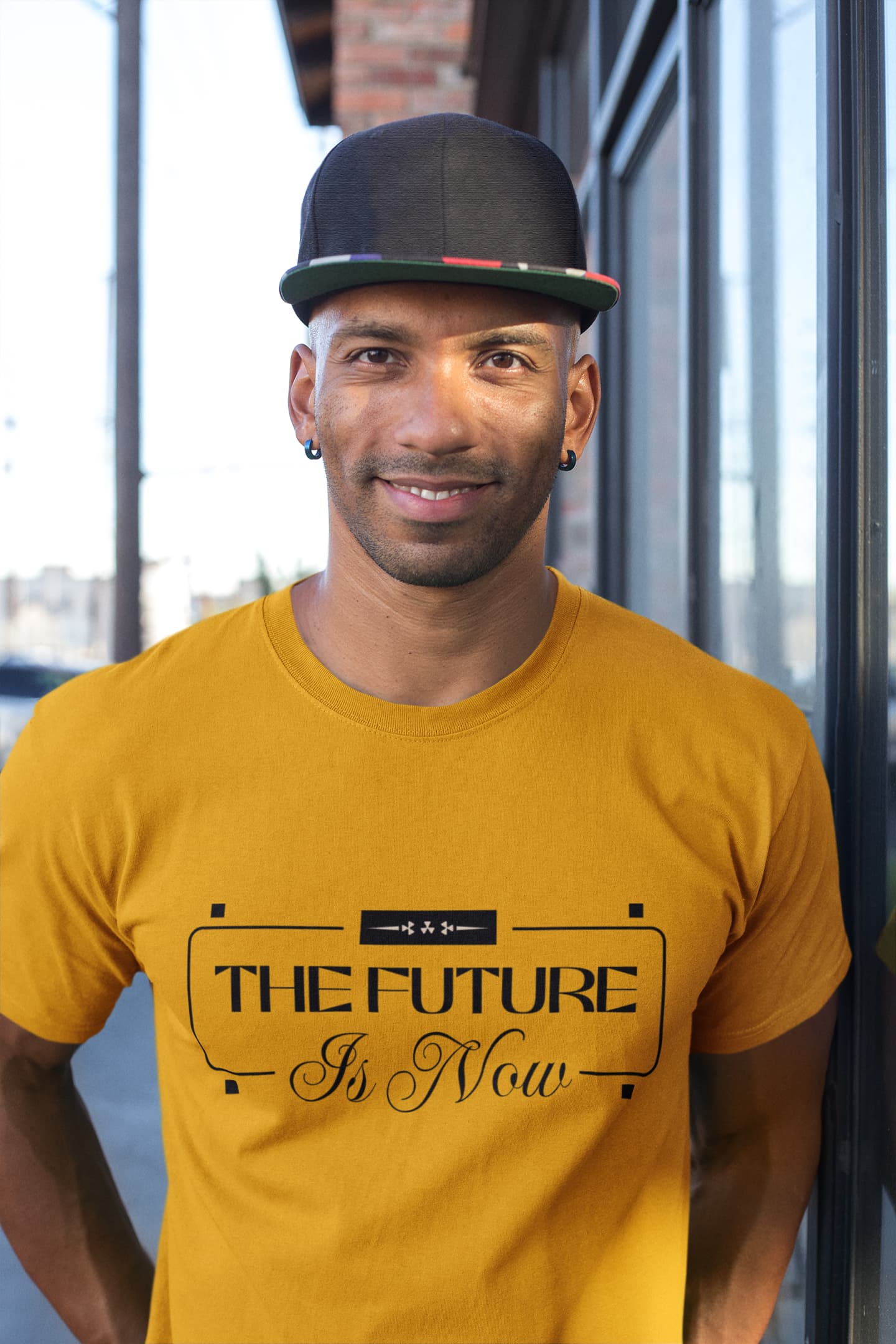 Man wearing a mustard yellow t-shirt with 'The Future Is Now' text, standing indoors.