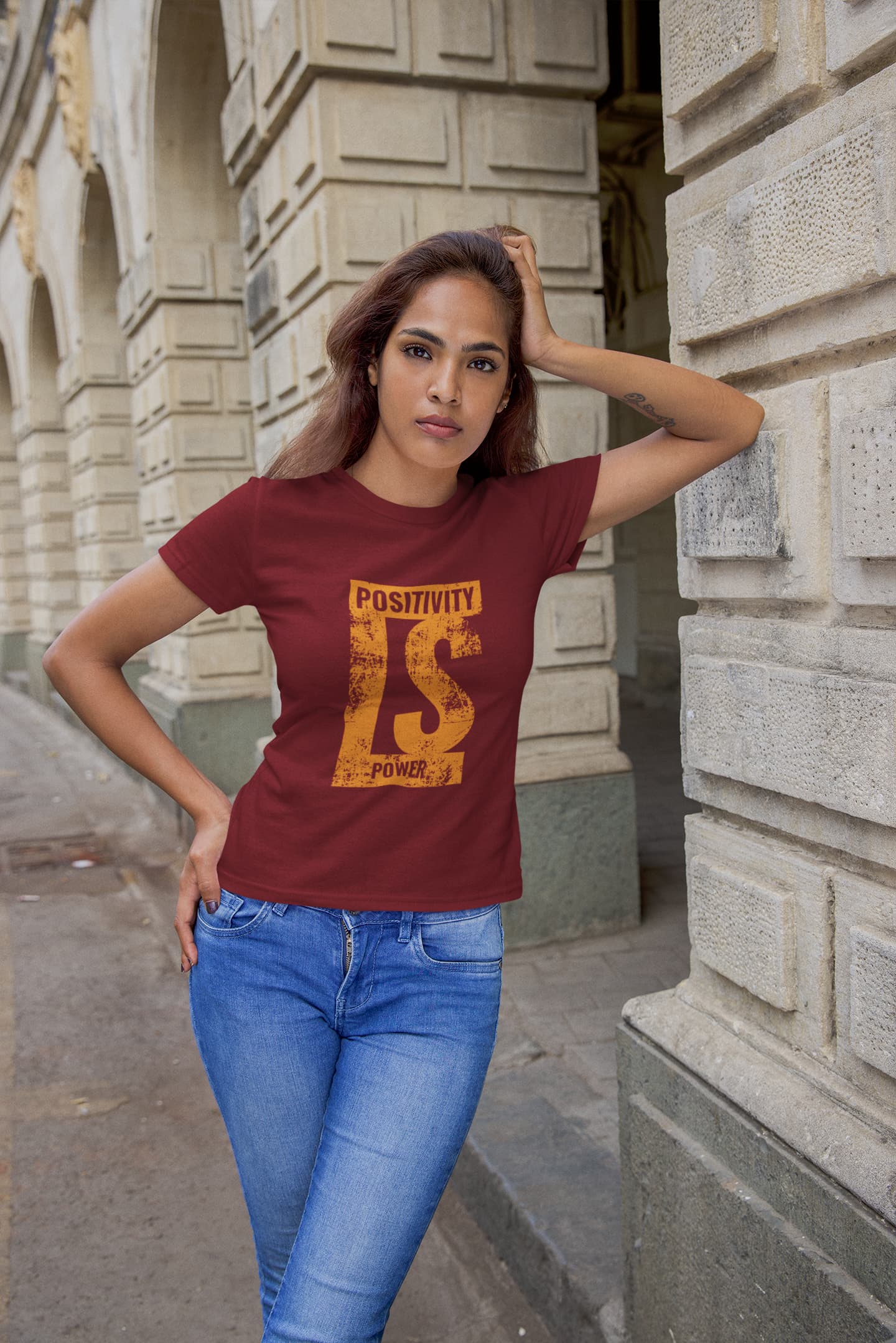 Woman wearing a maroon t-shirt with 'Positivity is Power' text in an urban setting.