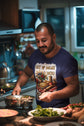 Man cooking in a kitchen wearing a colorful t-shirt.