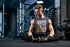 Man sitting on the floor in a gym wearing a tank top with text.