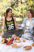 Two women enjoying a picnic in a park with food and drinks.
