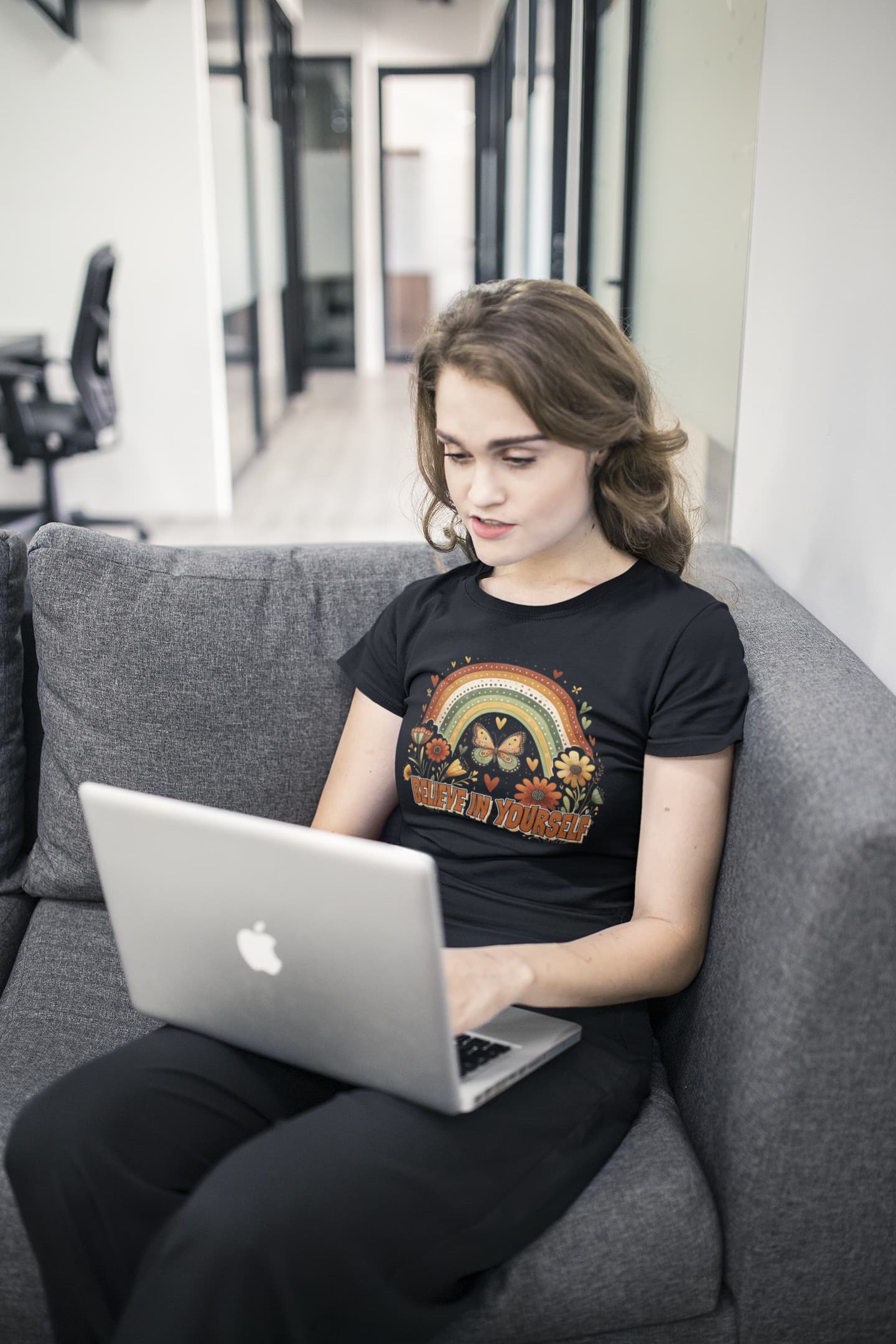 Person sitting on a couch using a laptop with a black t-shirt featuring a rainbow design.