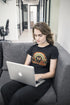 Person sitting on a couch using a laptop with a black t-shirt featuring a rainbow design.