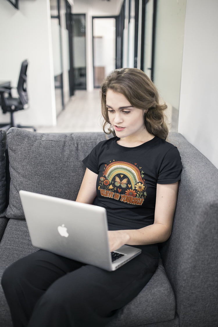 Person sitting on a couch using a laptop with a black t-shirt featuring a rainbow design.