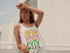 Woman wearing a white tank top with colorful text in an outdoor setting